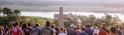 Ignite Texas retreat attendees gathered on a hillside facing a stone cross above a river